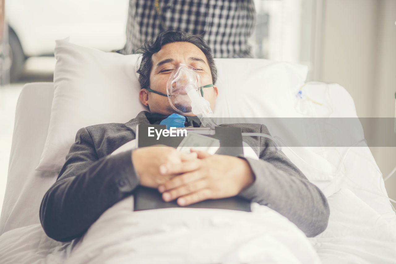 High angle view of patient with file and currency lying on bed in hospital