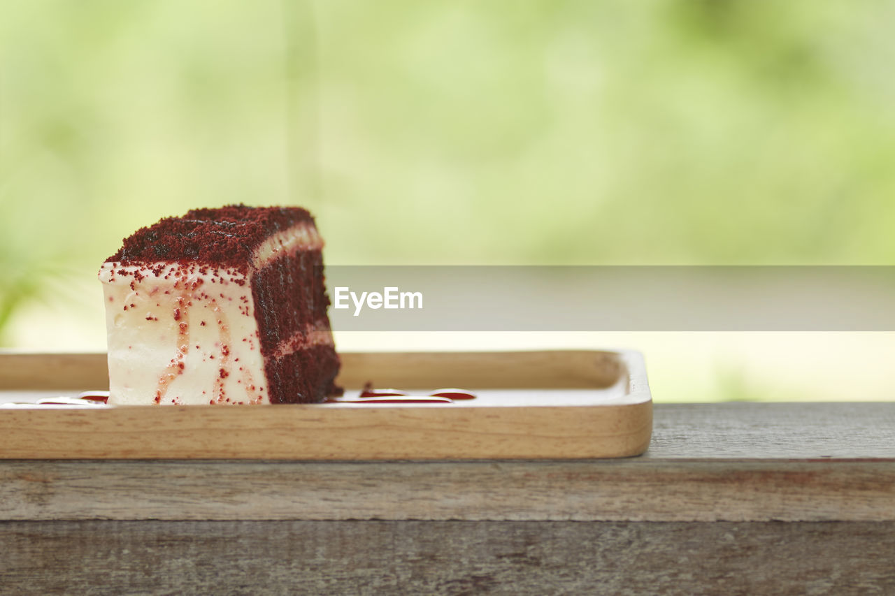 Close-up of red velvet cheesecake slice in wooden plate on table outdoors