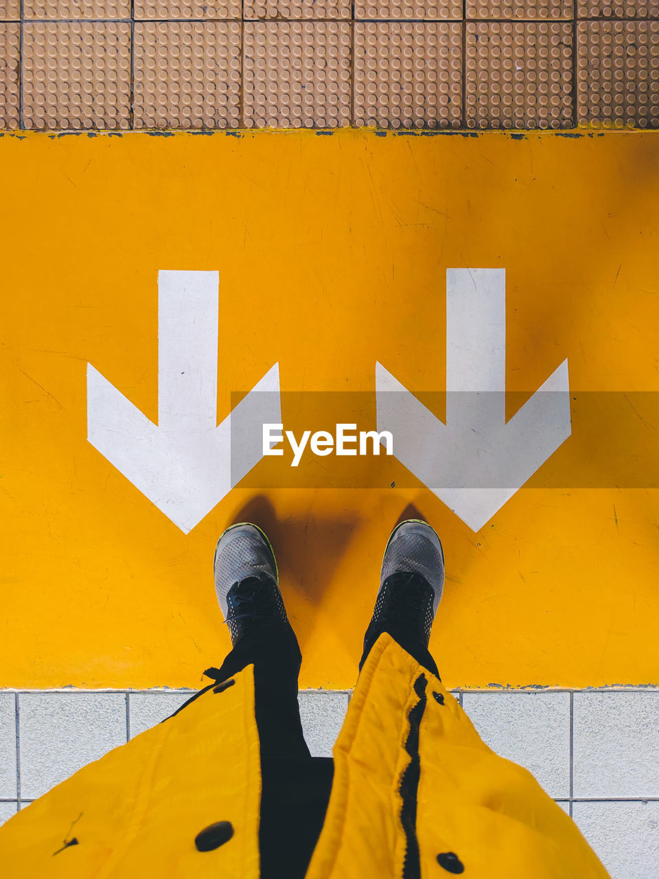 LOW SECTION OF PERSON WITH YELLOW ARROW SIGN ON ORANGE