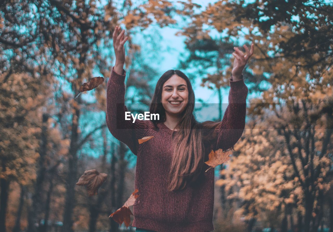 Portrait of smiling young woman standing in forest during autumn