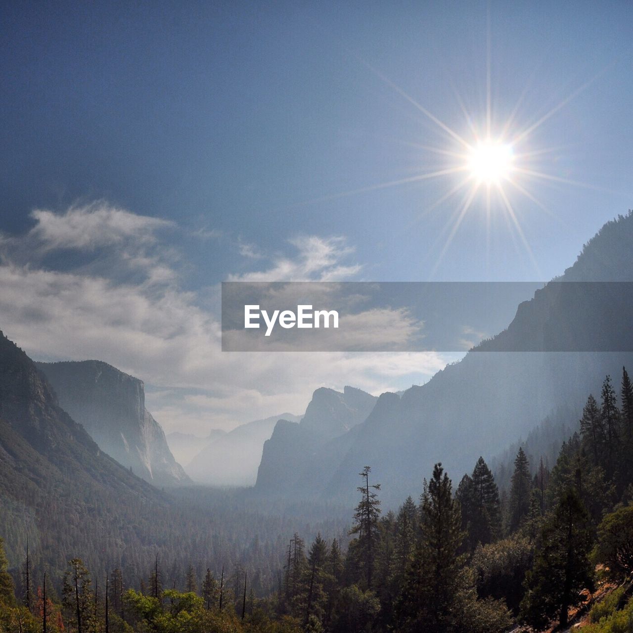 Scenic view of valley and mountains against cloudy sky on sunny day