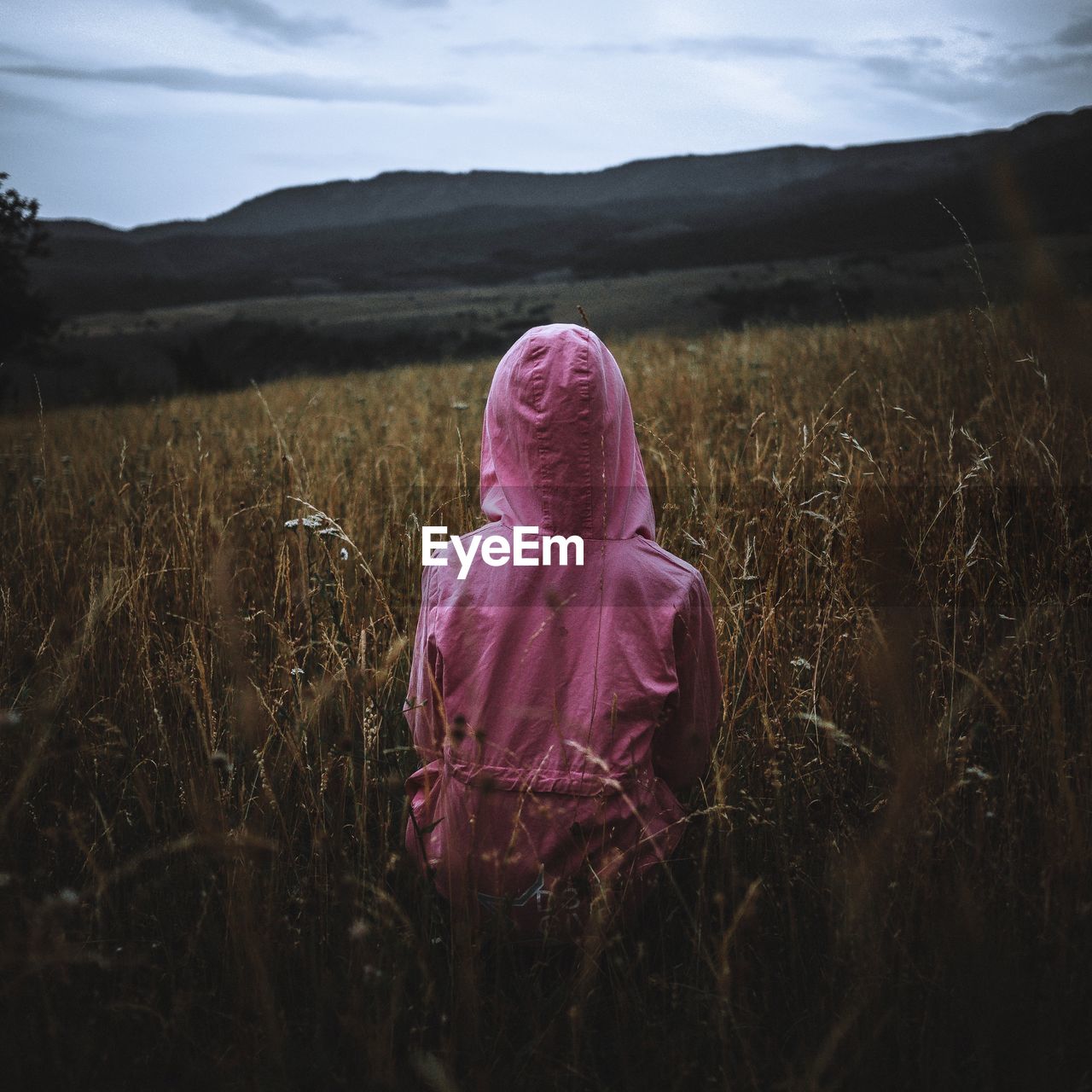 Rear view of girl wearing raincoat standing in field