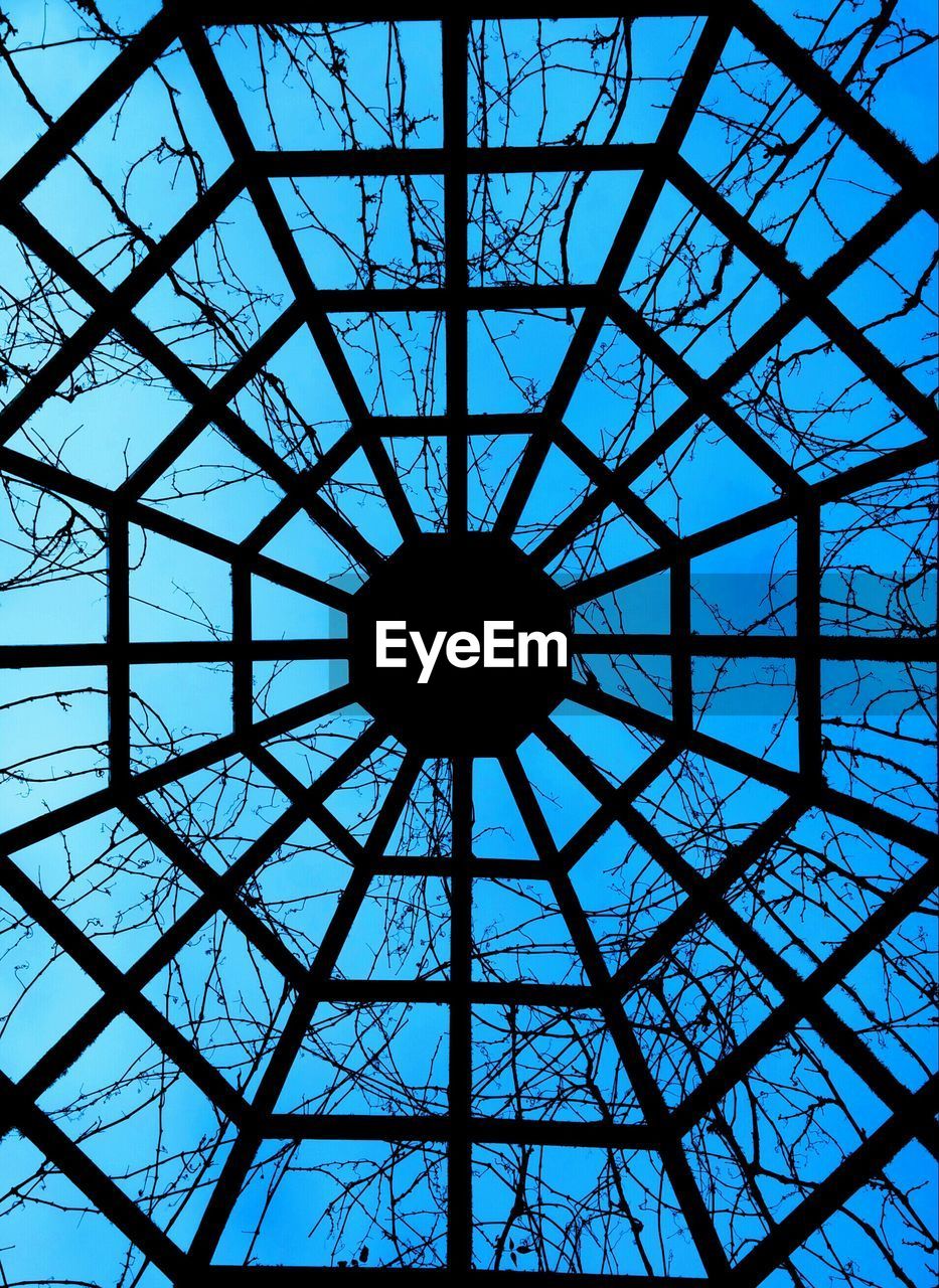 Directly below view of silhouette grid metal ceiling against blue sky with twigs