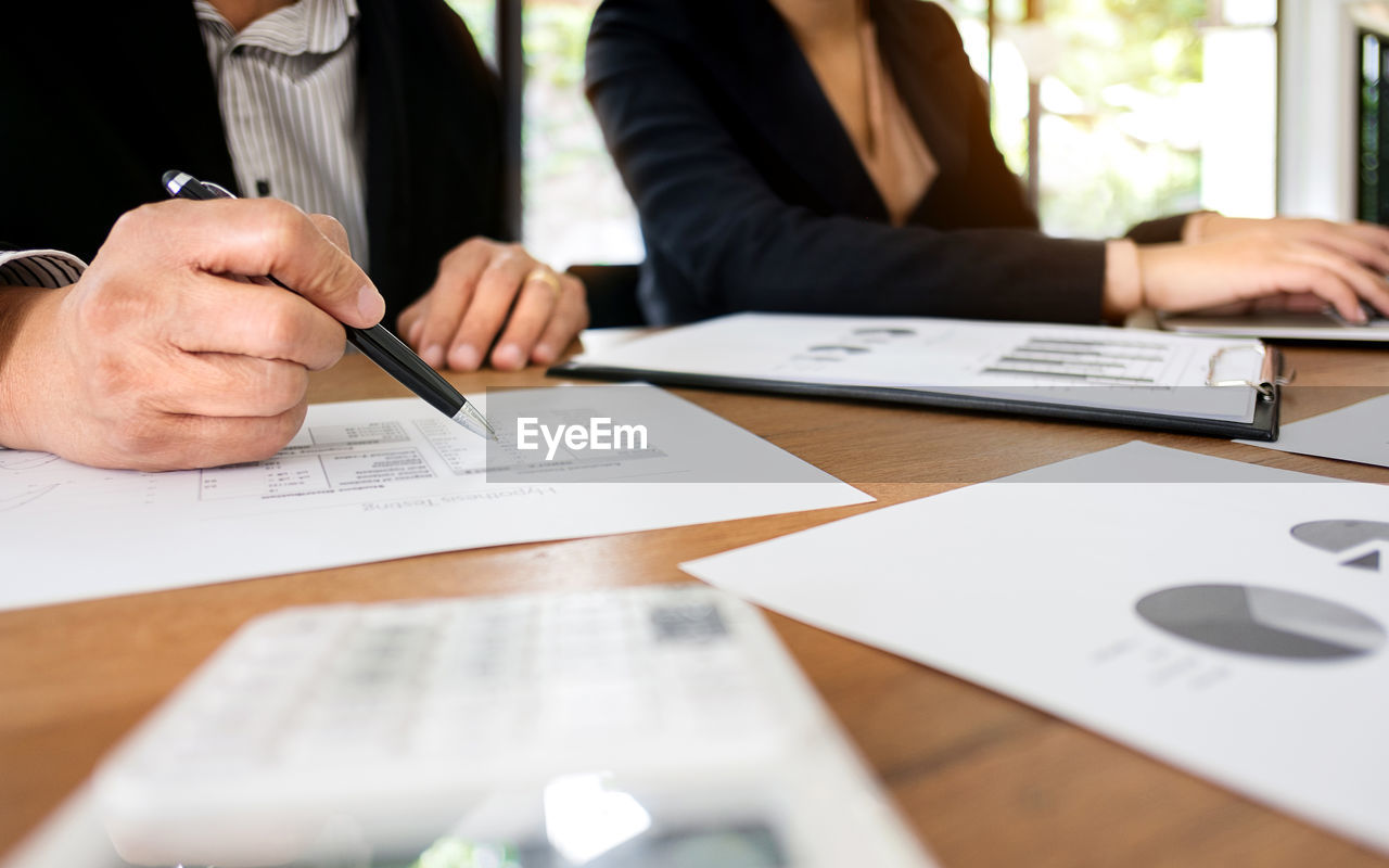 Midsection of colleagues working over graph in office