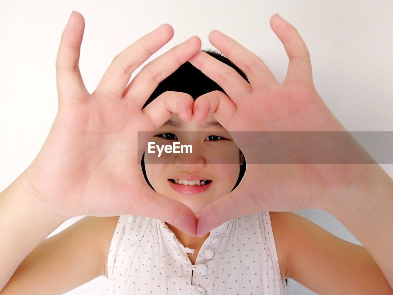 Close-up portrait of smiling girl making heart shape against wall