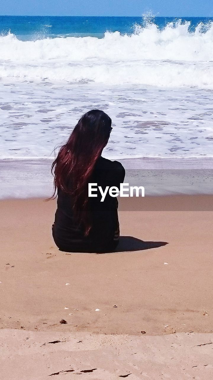 Rear view of woman sitting at beach on sunny day