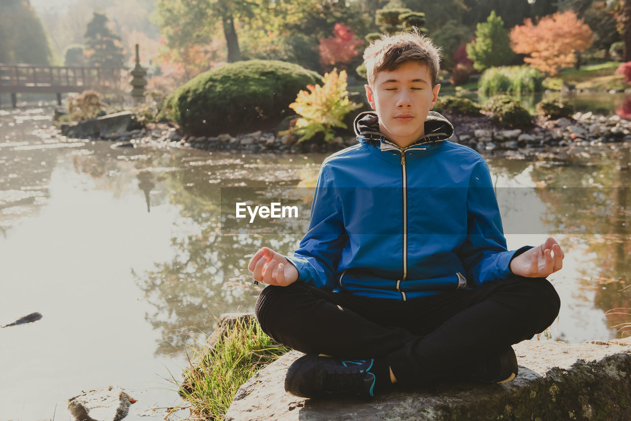 Teenage boy meditating and relaxing in a city park japanese garden. outdoor meditation