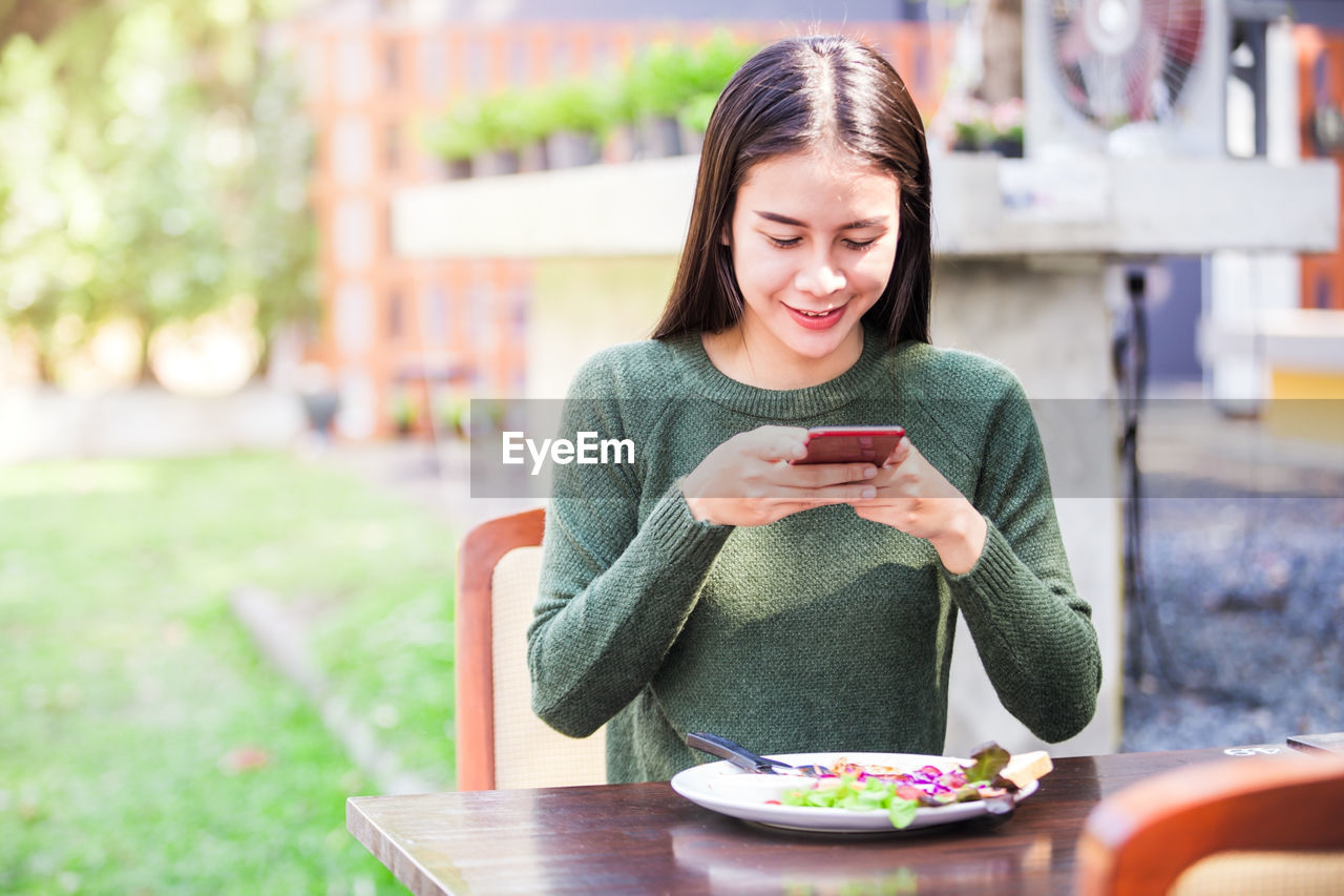 Young woman using mobile phone while sitting at table