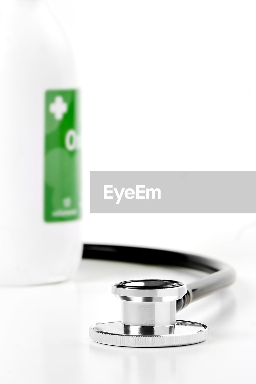 Close-up of stethoscope and bottle against white background