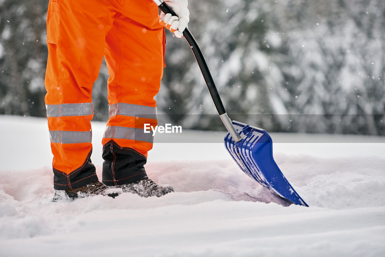 Low section of man with shovel standing on snow covered land