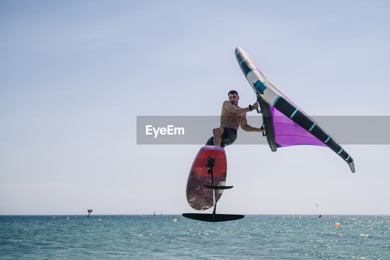 Shirtless young man with hydrofoil over sea on sunny day