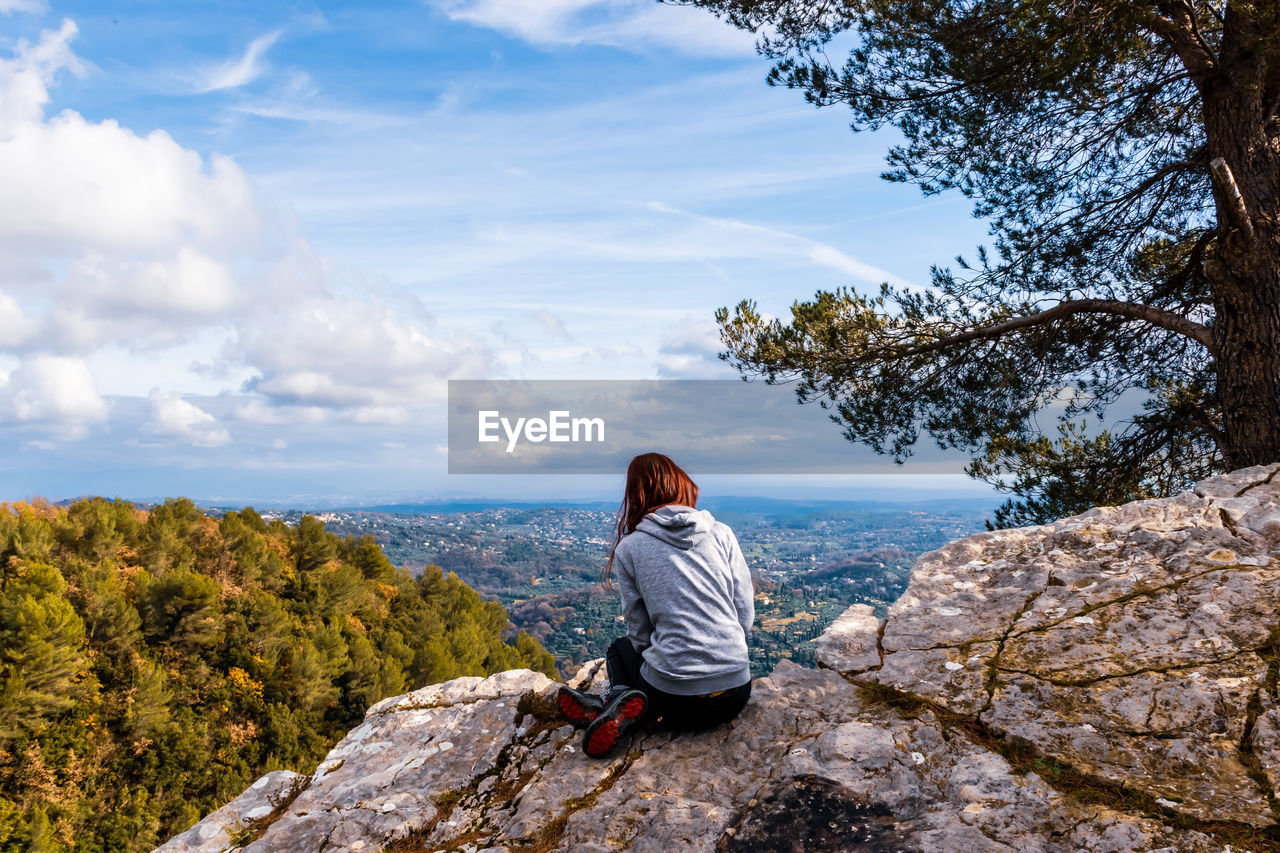 Woman sitting on rock looking at mountain against sky