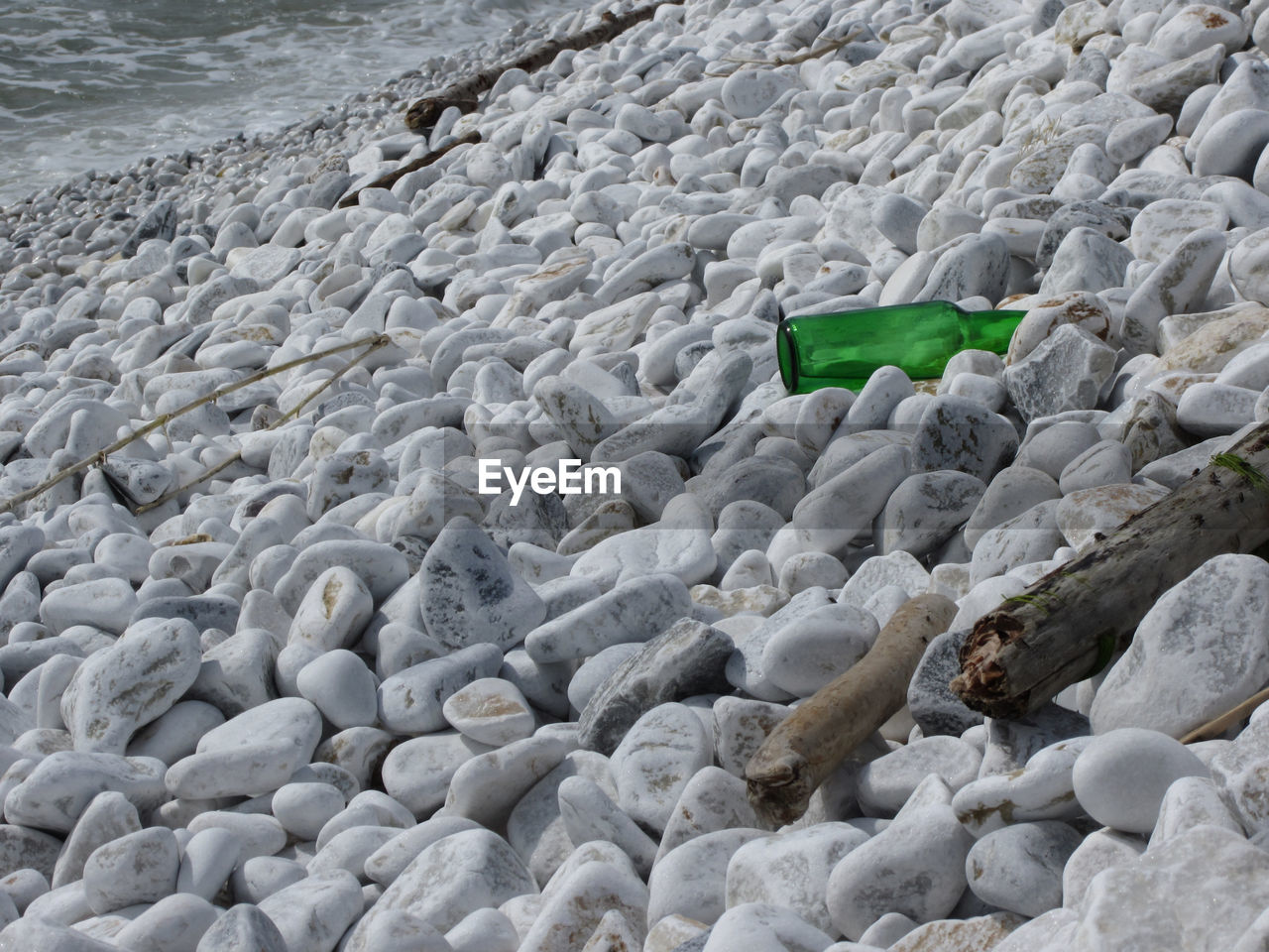 Garbage on the beach . particular of a green bottle abandoned between the pebbles