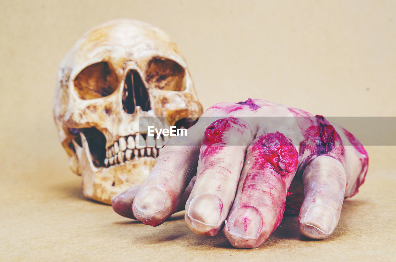 Close-up of hand and skull against beige background