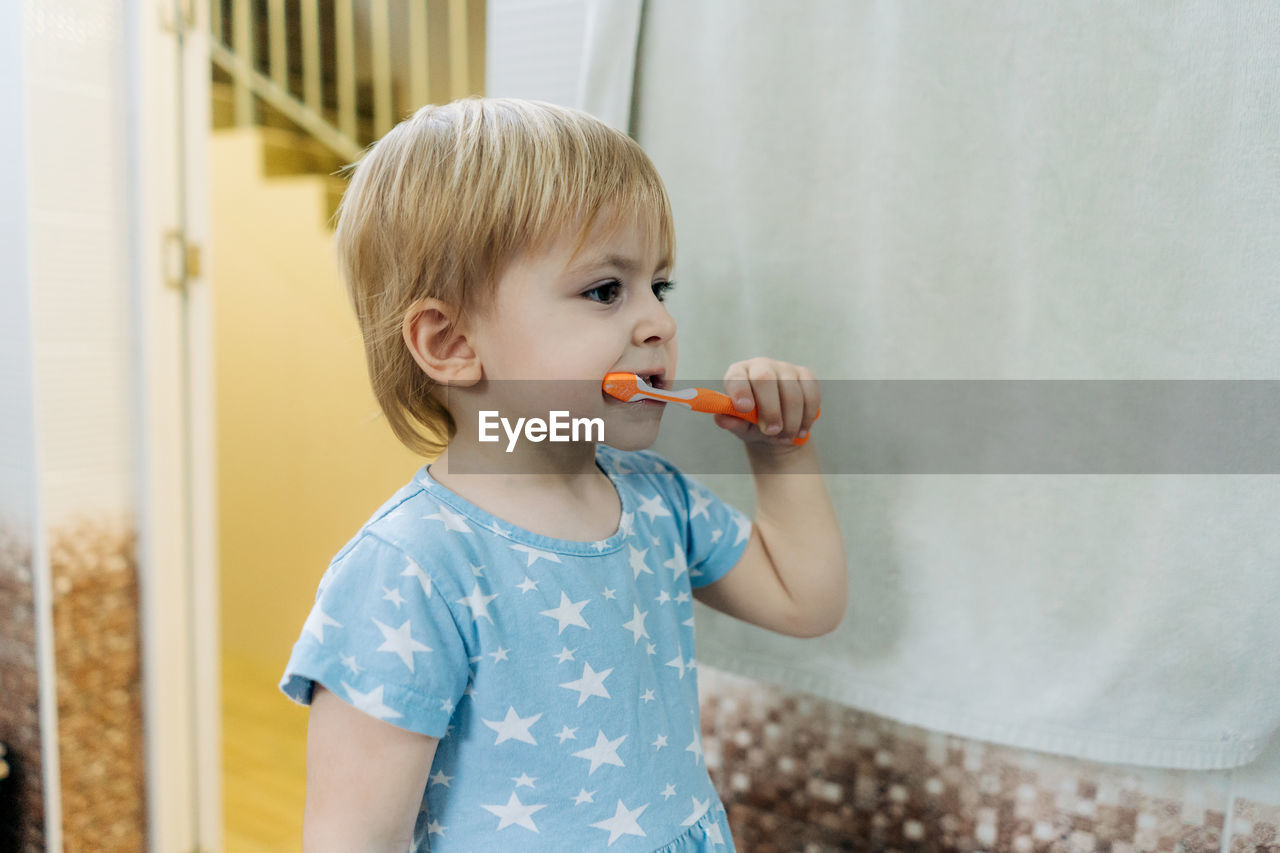 A little girl learns to brush her teeth on her own in the bathroom.