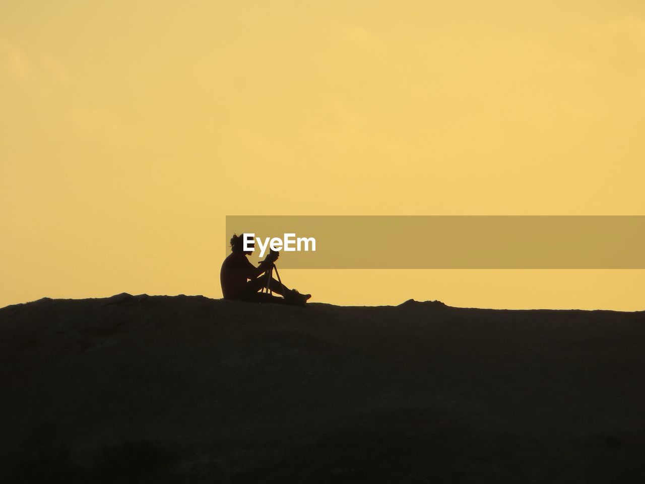 Silhouette man sitting on landscape against clear sky