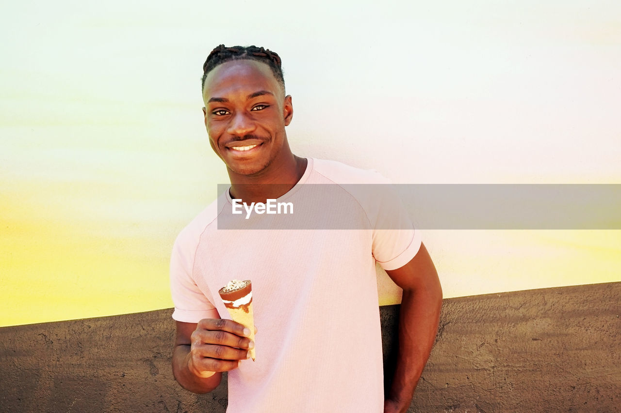 PORTRAIT OF SMILING YOUNG MAN HOLDING ICE CREAM OUTDOORS