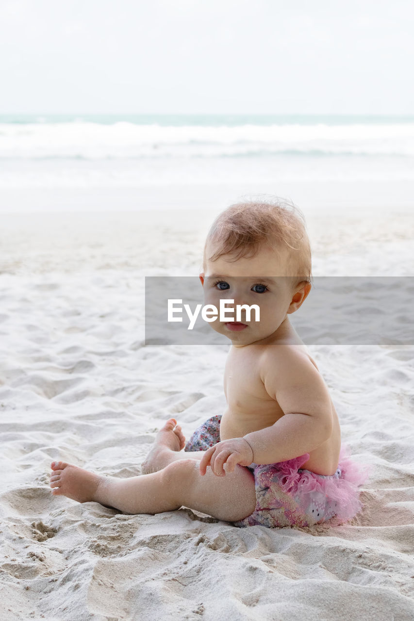 Candid portrait of adorable little baby girl on sand at beach on background of sea. 