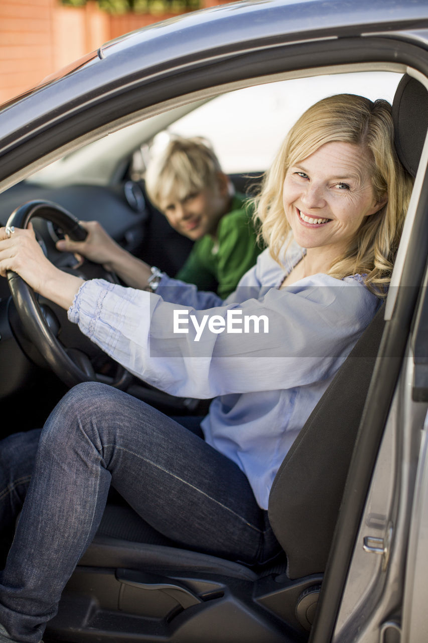 Portrait of happy woman driving car while sitting by son