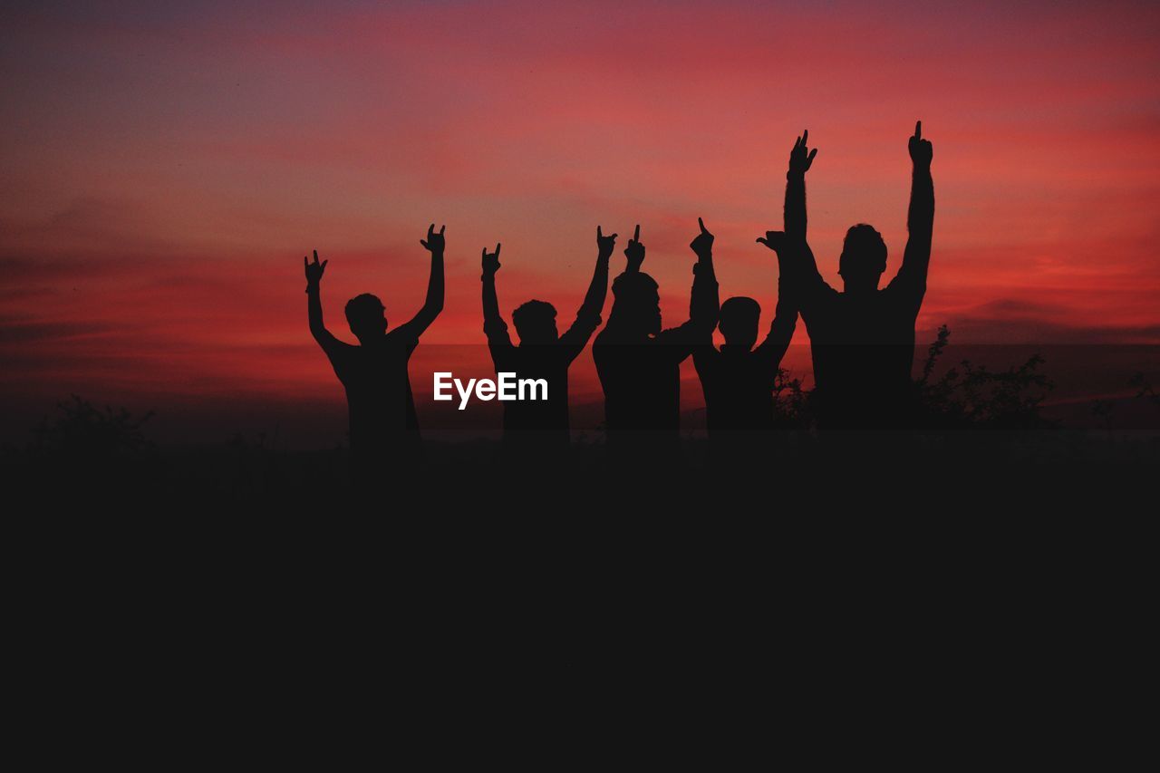 Silhouette people standing with arms raised against sky during sunset