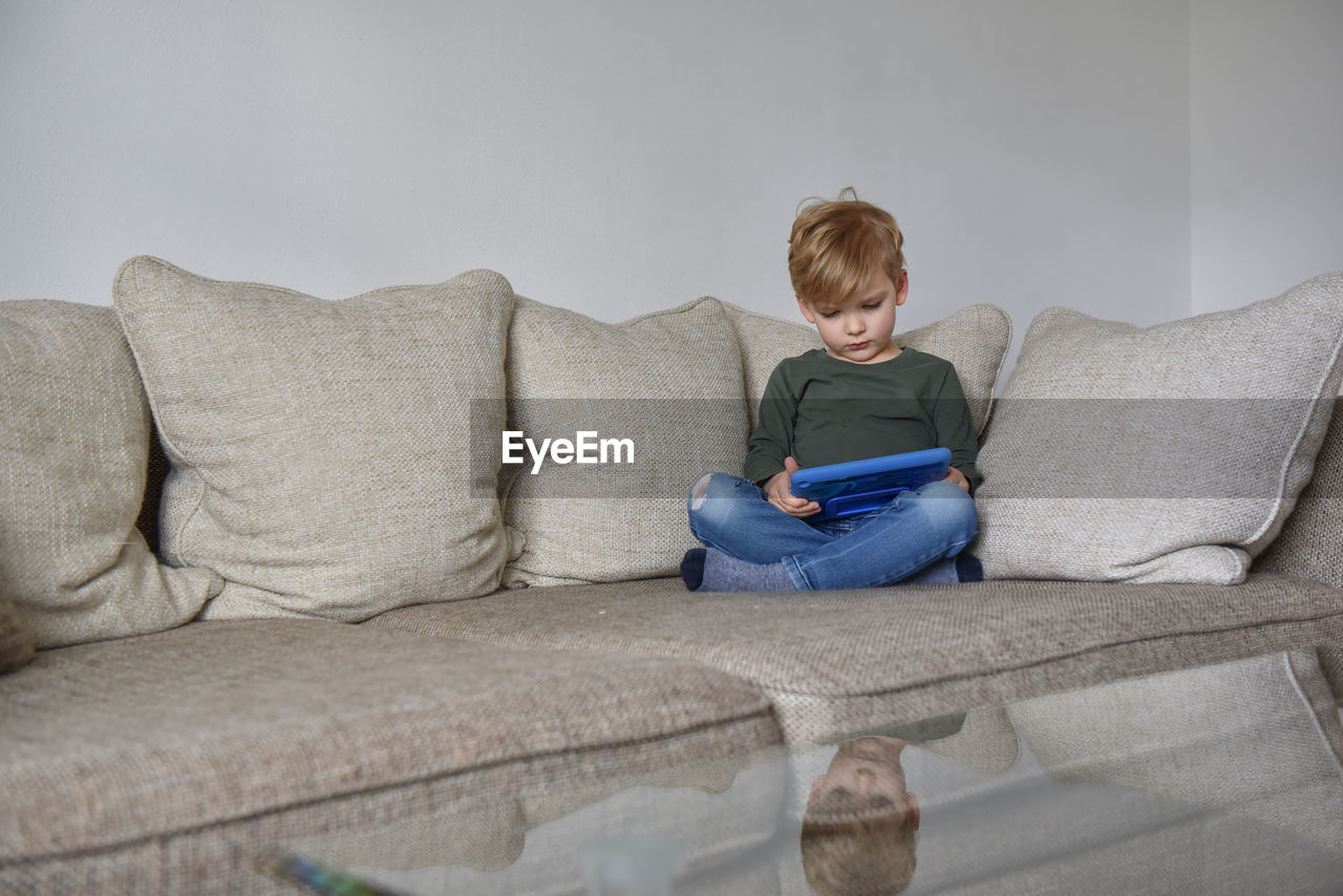 Boy sitting on sofa at home and playing tablet