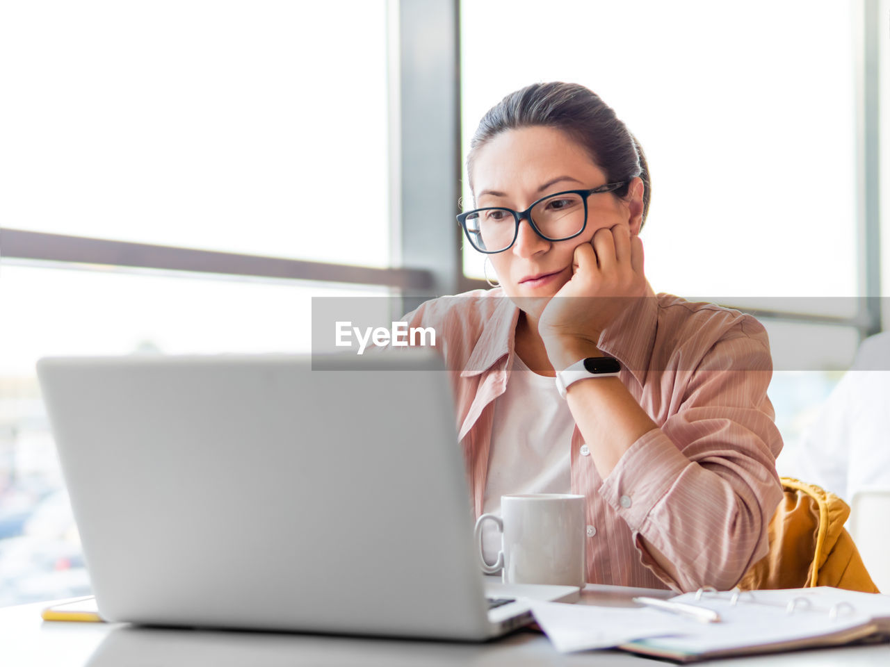 Frowned woman in eyeglasses works with laptop. co-working workplace for freelancers or students.