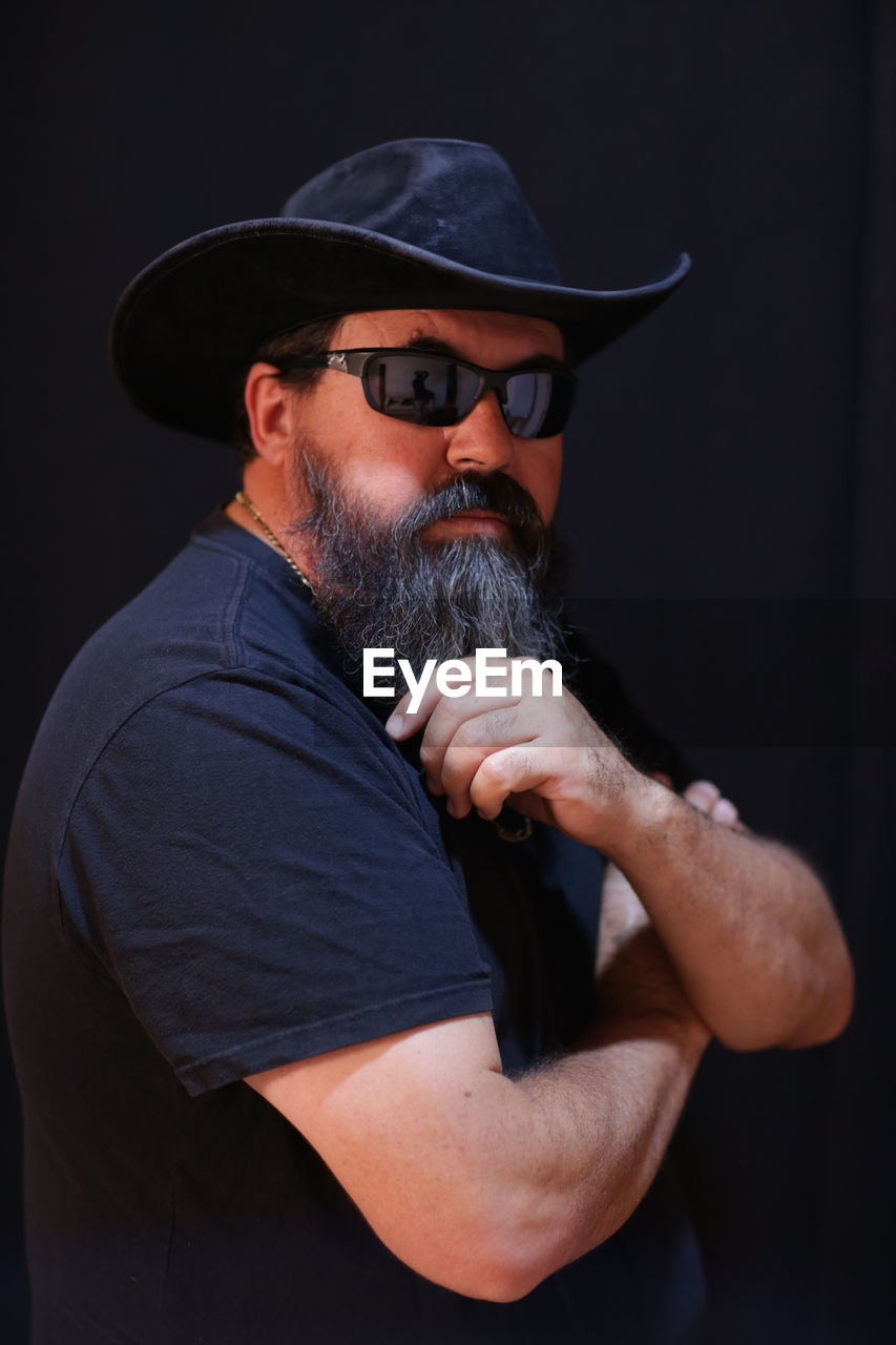 Portrait of bearded mature man wearing sunglasses against black wall