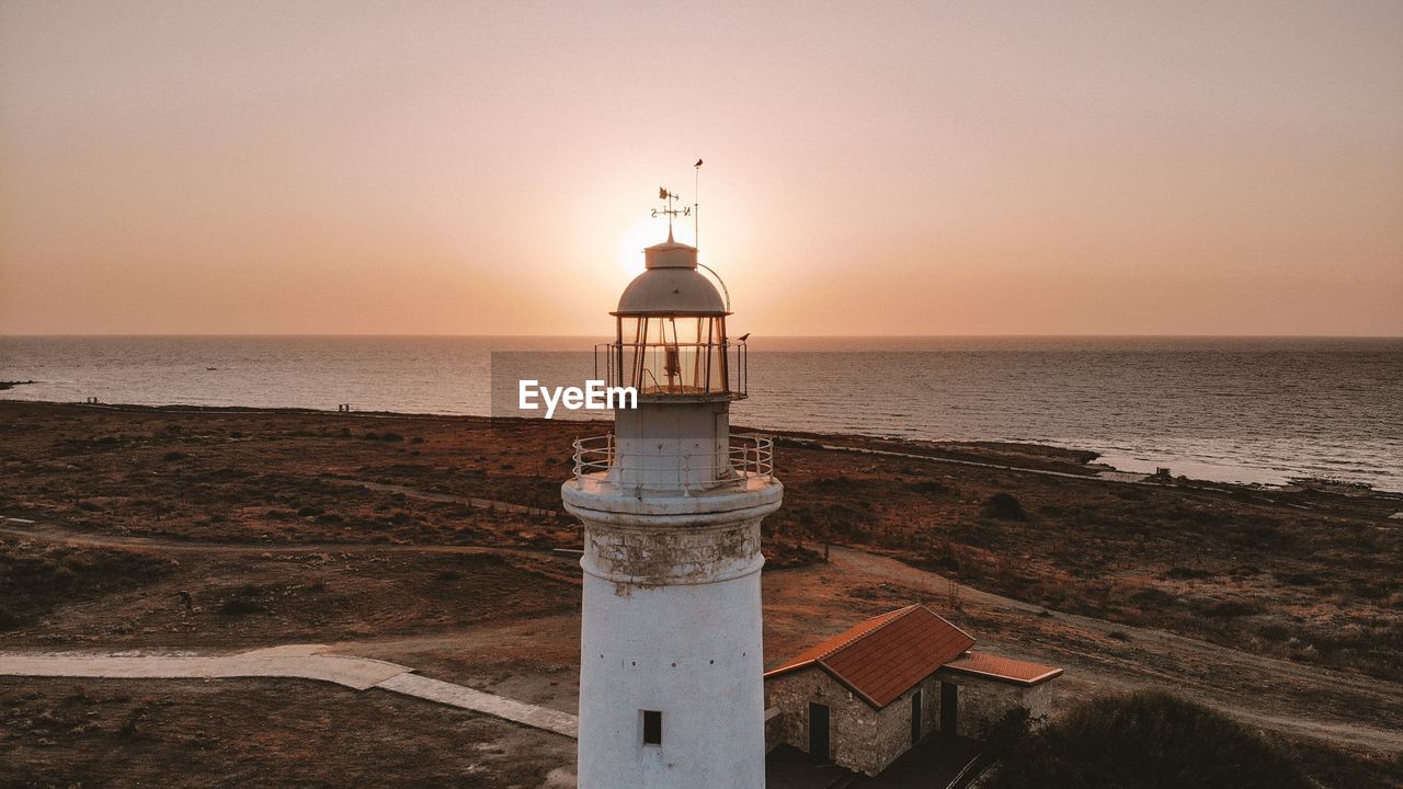 Lighthouse by sea against sky during sunset