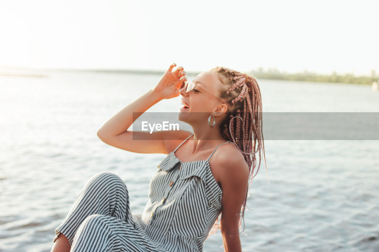 Happy young woman sitting against lake