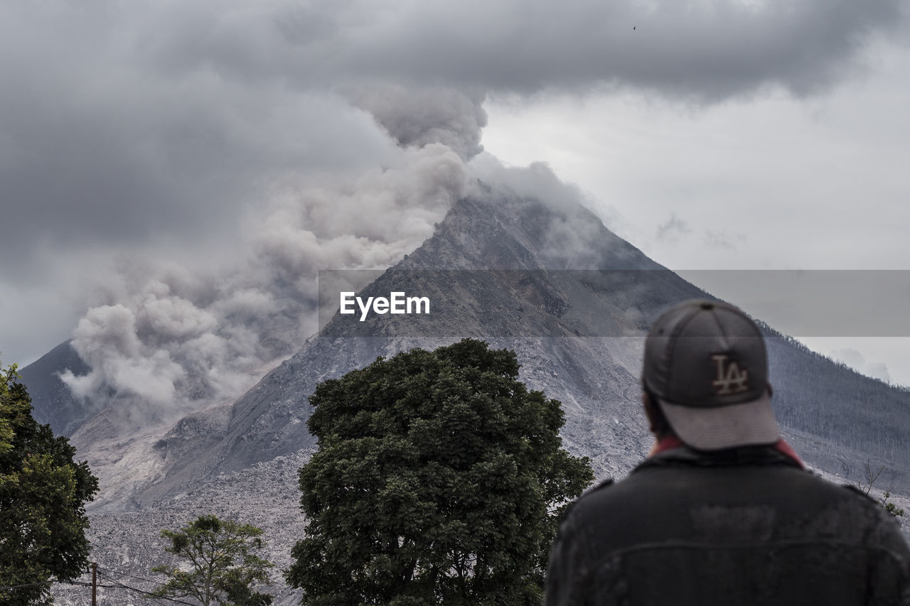 REAR VIEW OF MAN ON MOUNTAIN AGAINST SKY