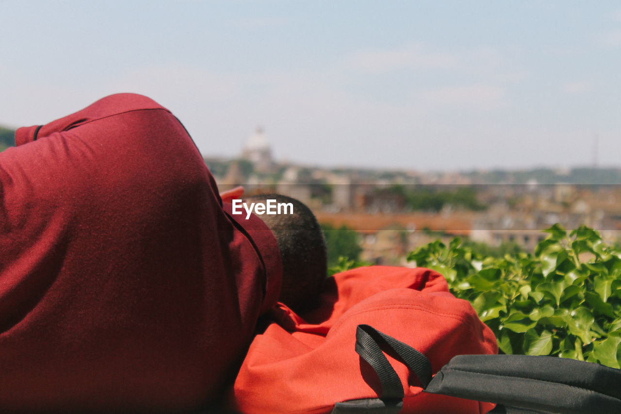 Rear view of man sleeping on backpack against sky