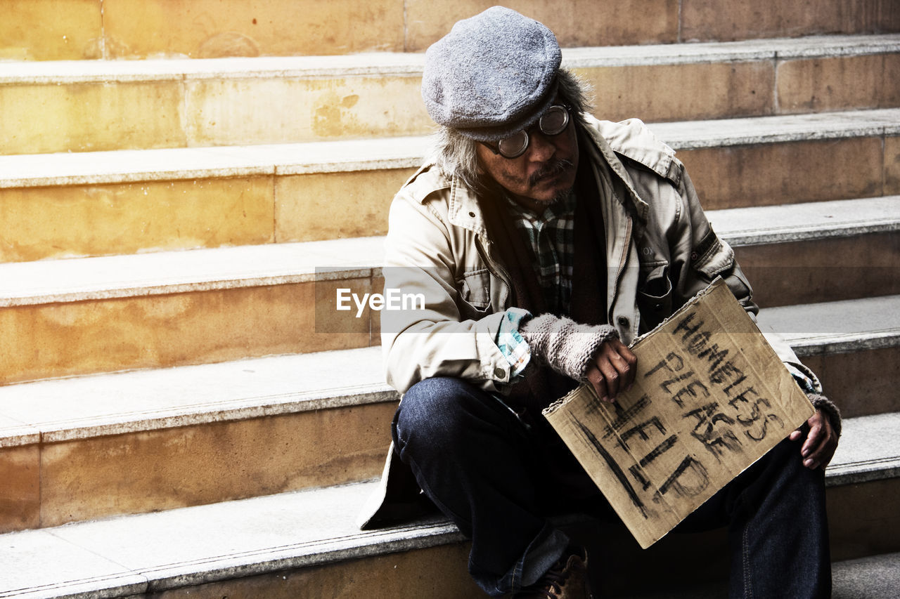 Homeless man holding sign while sitting on steps