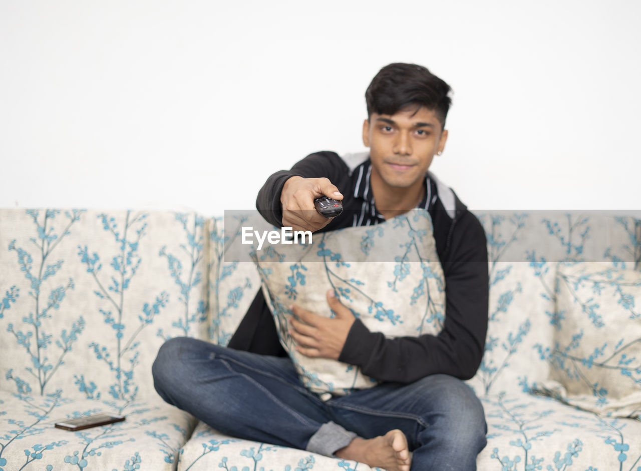 A teenage boy with happy face is sitting on the sofa with a remote from the tv. self- isolation.