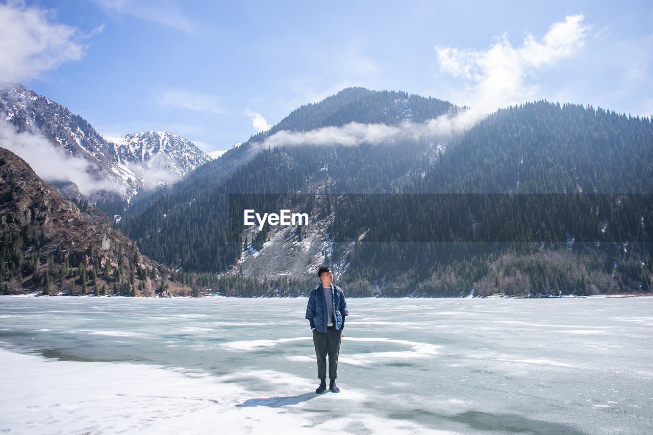 Man standing on frozen lake against mountains and sky