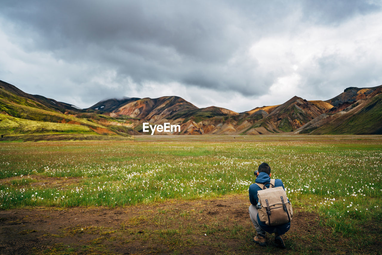 Hiker photographing valley and mountains against cloudy sky