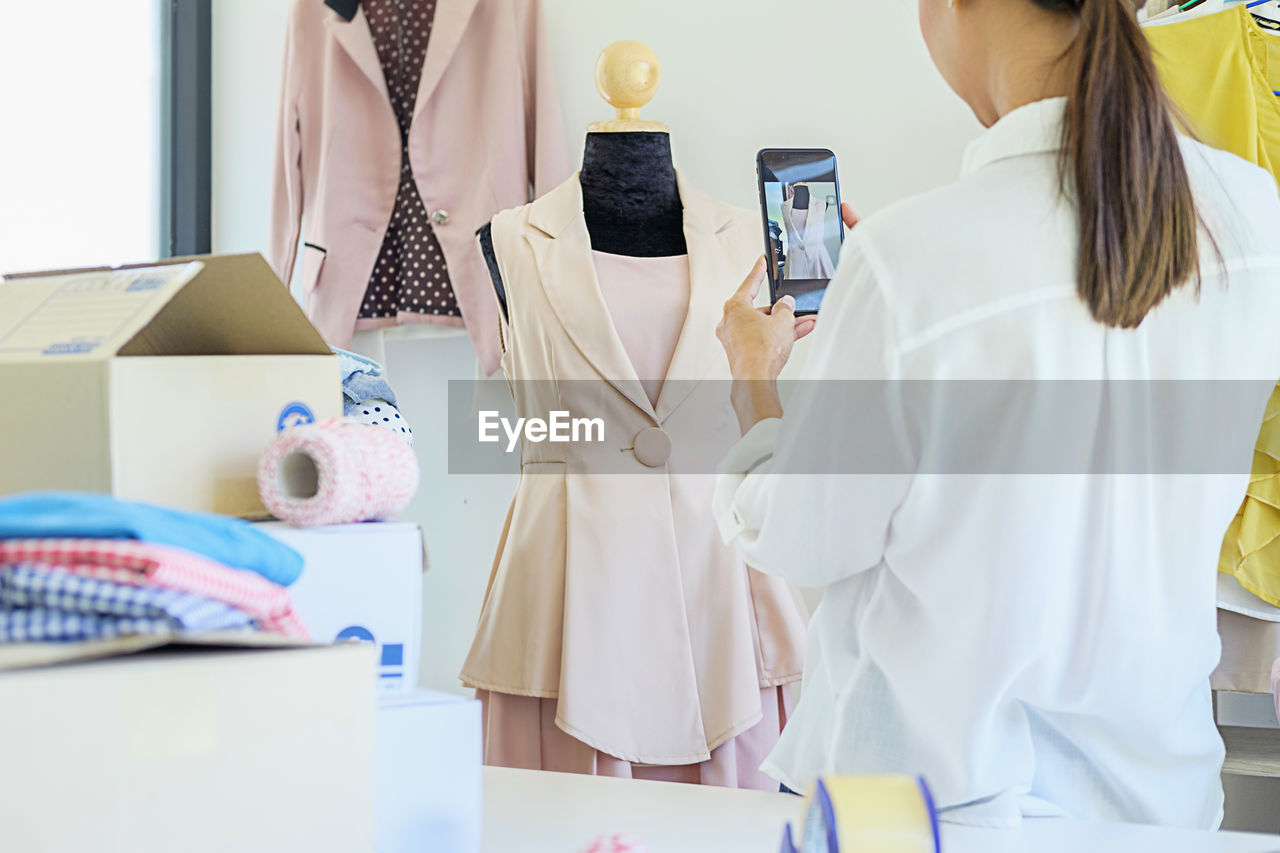 Rear view of fashion designer photographing dress on mannequin in office