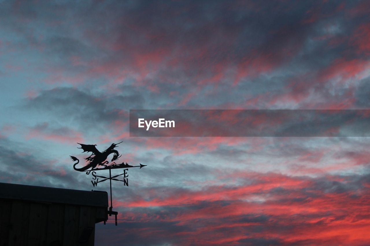 Silhouette of weather vane against cloudy sky