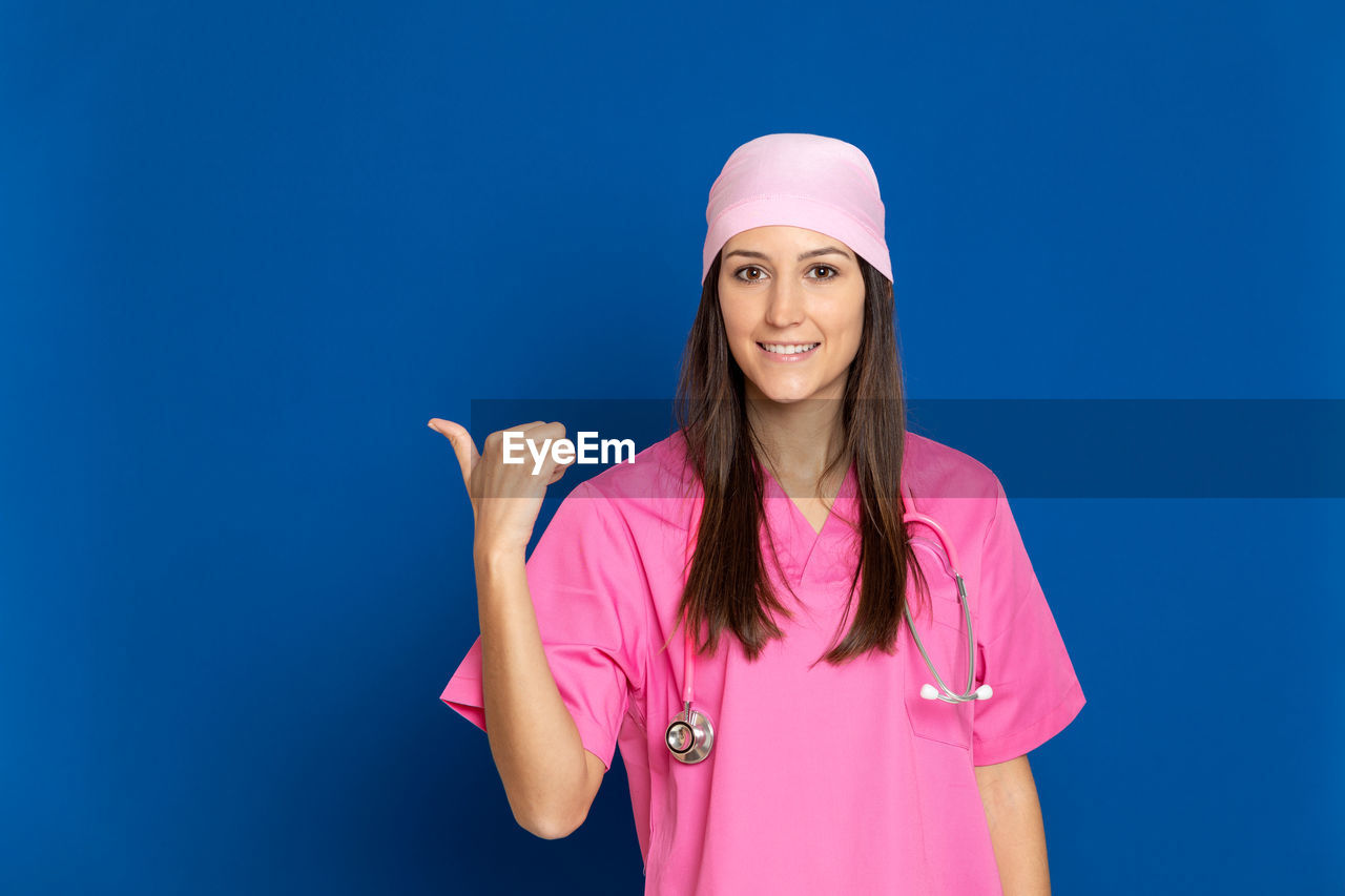 PORTRAIT OF HAPPY WOMAN STANDING AGAINST BLUE BACKGROUND