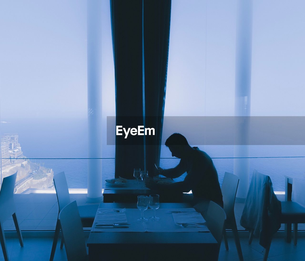 Young man eating food while sitting at table by window in restaurant