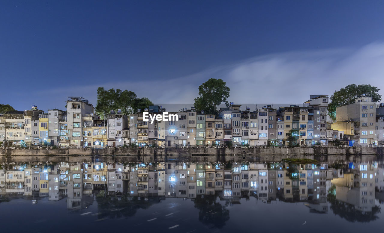 Buildings by lake against sky in city at night