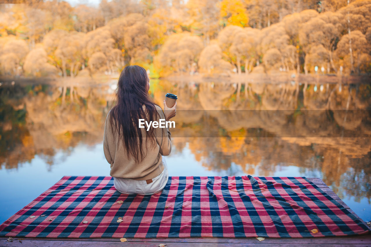 REAR VIEW OF WOMAN PHOTOGRAPHING AGAINST TREE