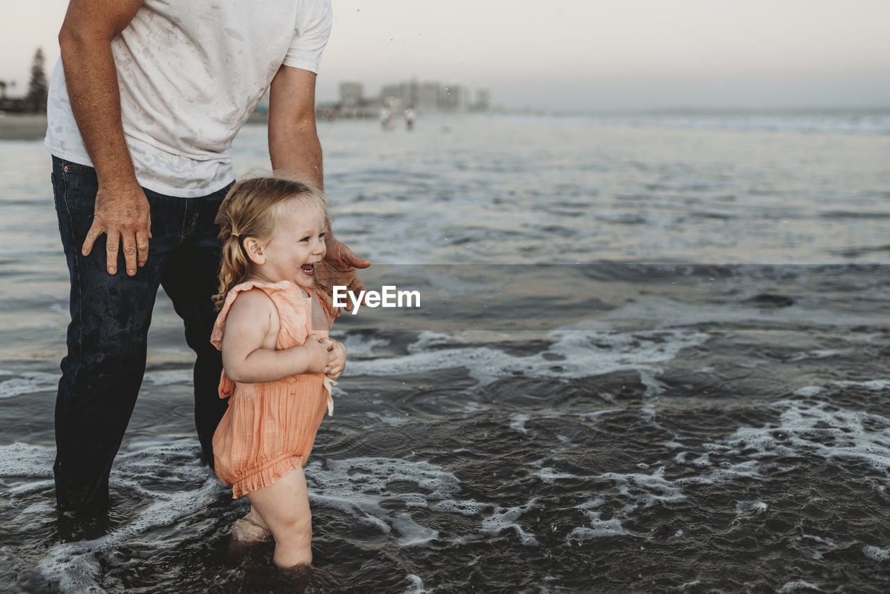 Toddler girl splashing in ocean with father at sunset