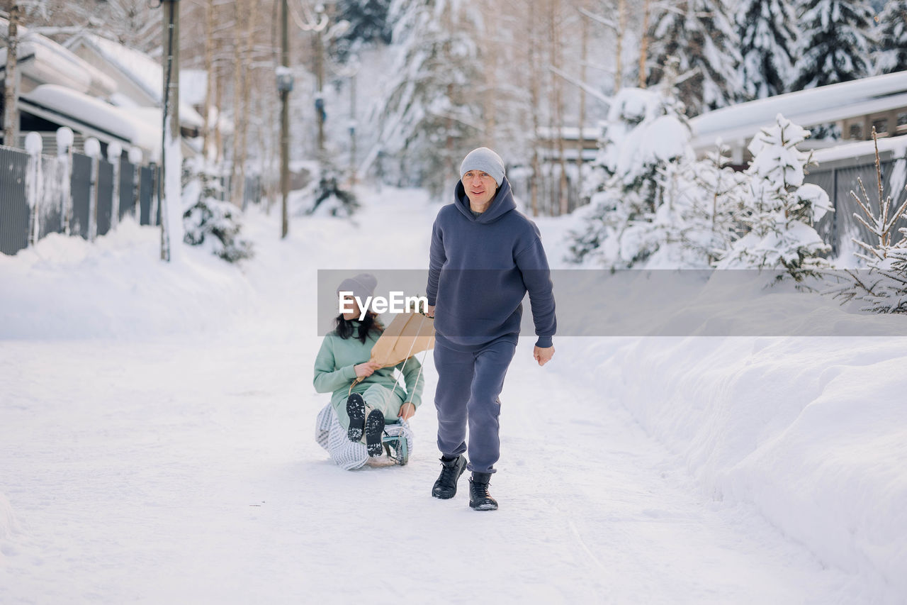 Smiling man giving sledding ride to woman. love and leisure concept.