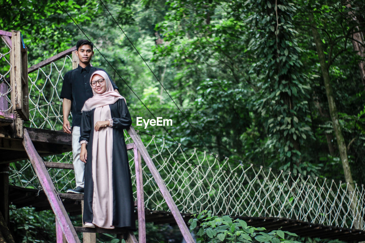 Man and woman on footbridge against trees in forest