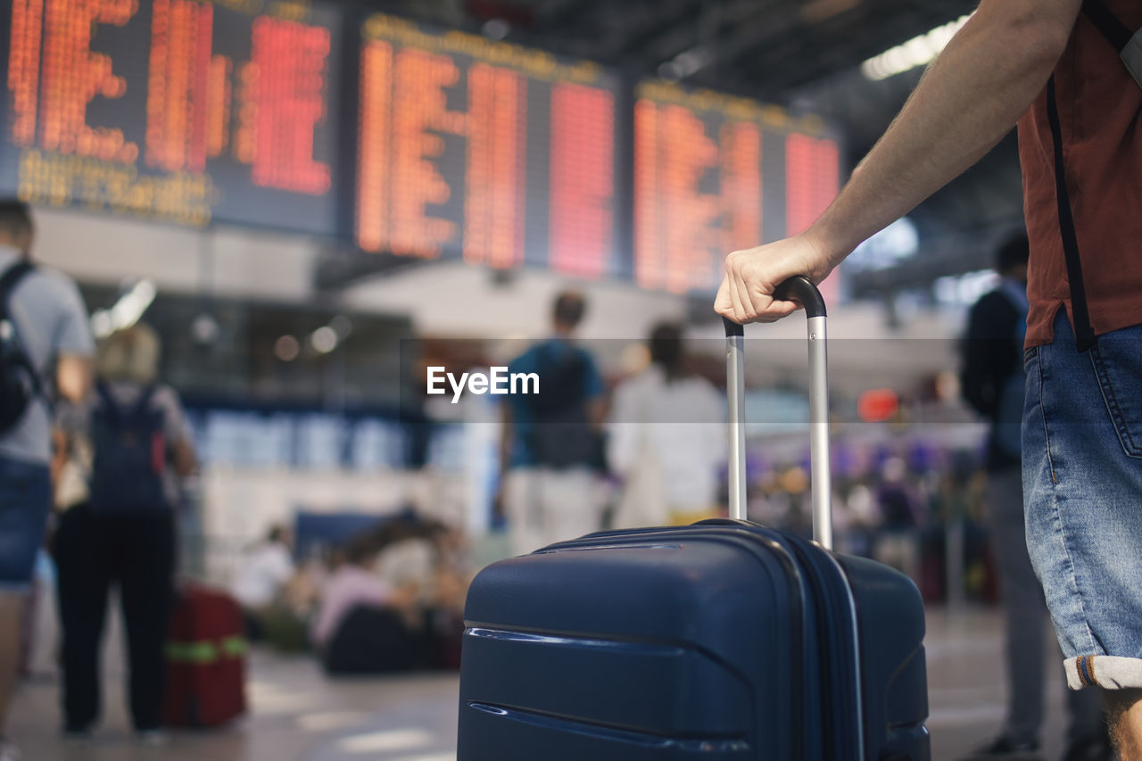 Traveling by airplane. man waiting in airport terminal. selective focus on hand holding suitcase.