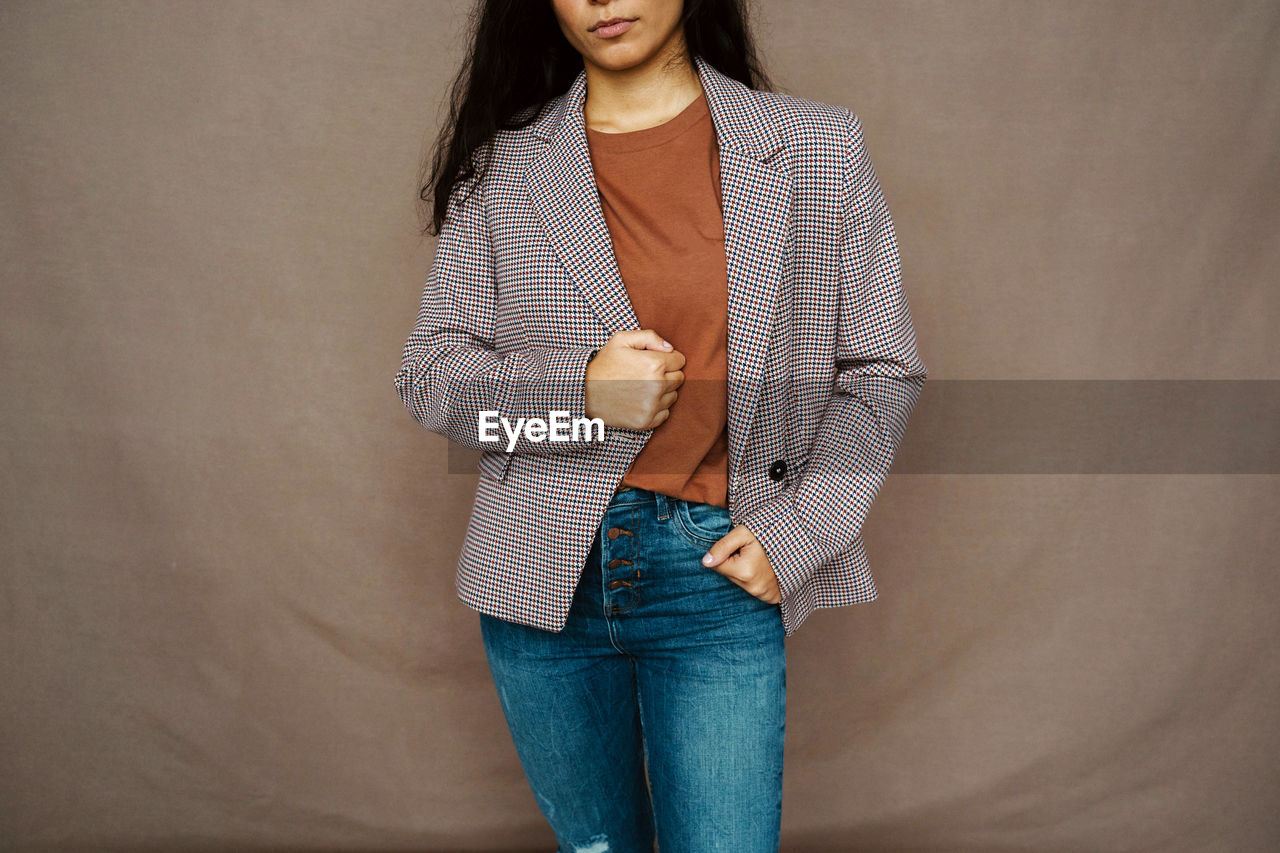 Cropped unrecognizable female in casual jacket standing on brown background in studio