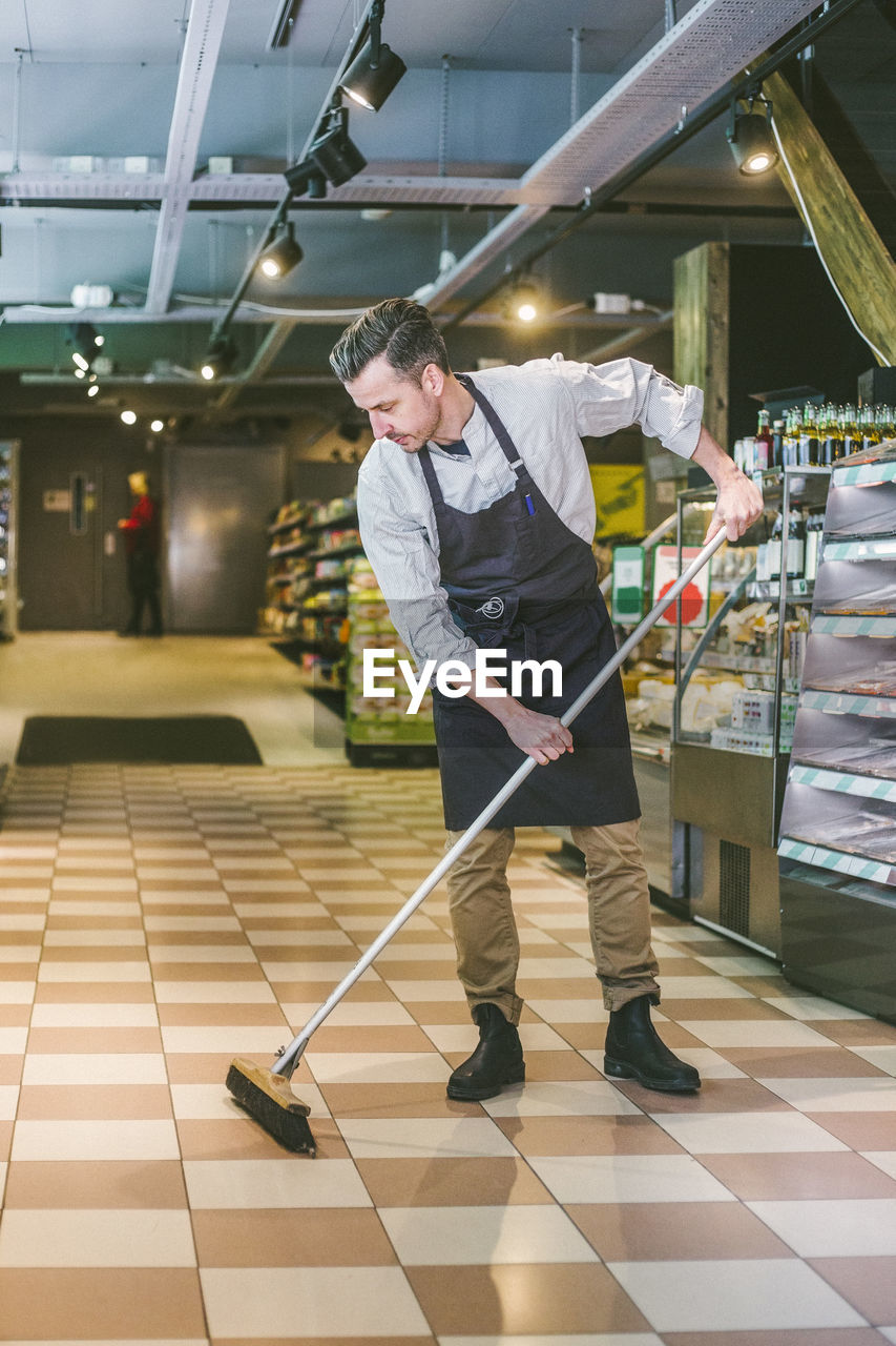 Full length of salesman sweeping floor in grocery store