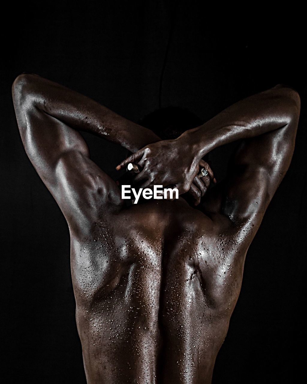 Rear view of shirtless muscular man with sweat standing against black background
