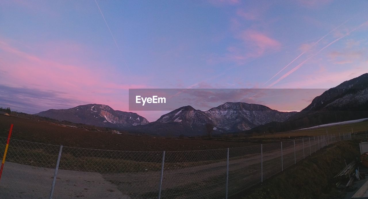 Fence on landscape against sky during sunset