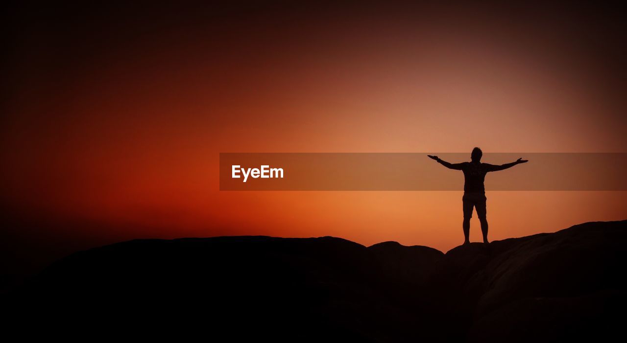 Silhouette man with arms outstretched standing against sky during sunset